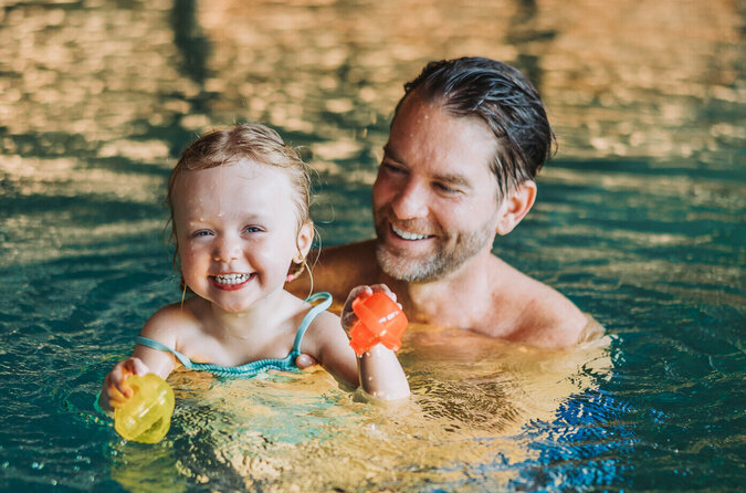 Vater und Tochter genießen lachend ihre Zeit im Pool Vater und Tochter lachen zusammen im Pool eines Kinderhotels.