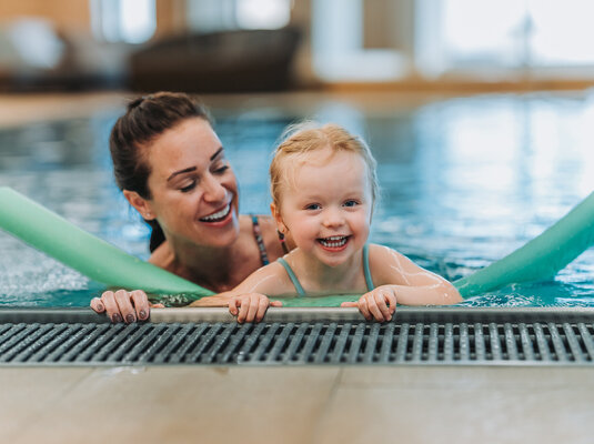Mutter und Tochter genießen den Pool mit Schwimmnudel im Kinderhotel Mutter und Tochter spielen lachend im Pool mit einer Schwimmnudel.