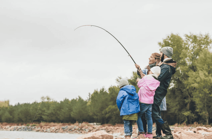 Familie beim Fischen am See während des Natururlaubs Eine Familie angelt gemeinsam an einem ruhigen Seeufer, umgeben von Natur.