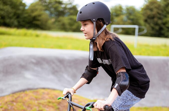 Fahrspaß mit Sicherheit – so macht Urlaub auf zwei Rädern richtig Freude. Kind mit Fahrradhelm und Schutzausrüstung fährt fröhlich auf einem Fahrrad im Freien.