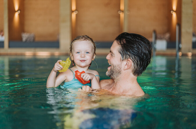 Vater und Tochter verbringen fröhliche Zeit im Pool des Familienhotels Vater und Tochter lachen gemeinsam beim Baden im Pool eines Familienhotels.