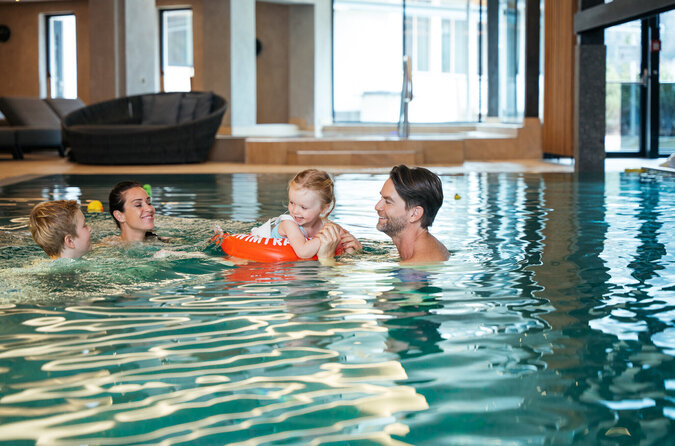 Familie hat Spaß gemeinsam im Pool des Kinderhotels Eine Familie mit Eltern und Kindern spielt lachend zusammen im Pool.