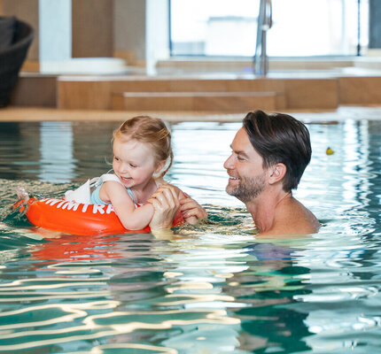 Familie hat Spaß gemeinsam im Pool des Kinderhotels Eine Familie mit Eltern und Kindern spielt lachend zusammen im Pool.