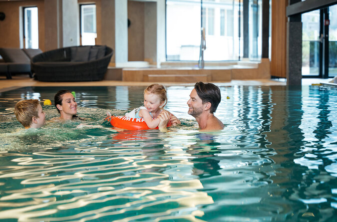 Familie hat Spaß gemeinsam im Pool des Kinderhotels Eine Familie mit Eltern und Kindern spielt lachend zusammen im Pool.