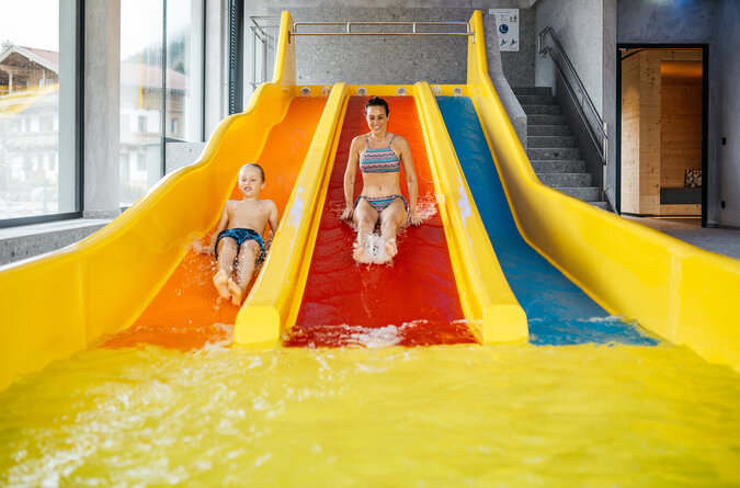 Mama und Sohn rutschen gemeinsam auf der Indoor-Wasserrutsche Mutter und Sohn rutschen gemeinsam auf einer Indoor-Wasserrutsche in einem Kinderhotel.